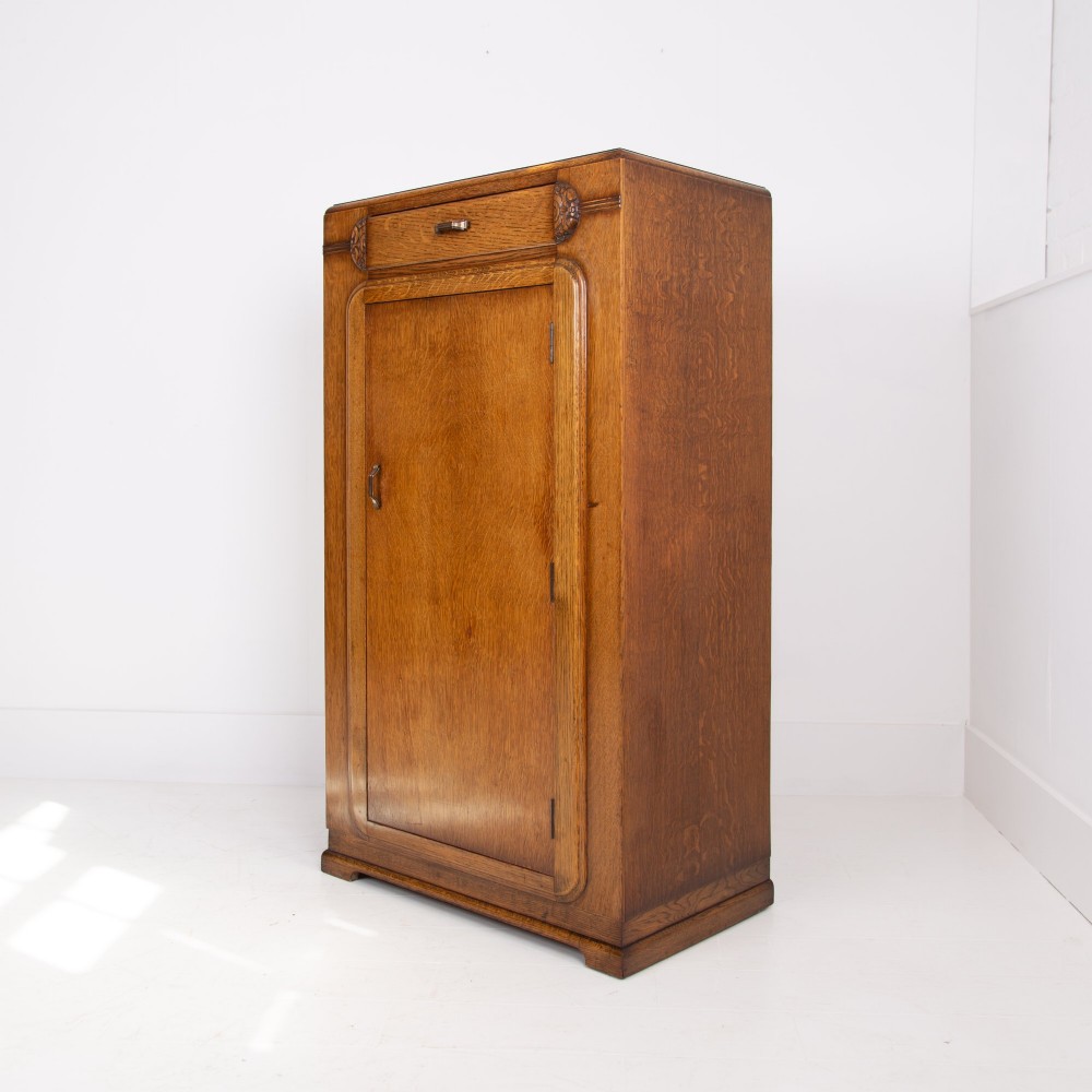 A 1930s Art Deco oak bachelors wardrobe featuring a top drawer, a central cupboard door with rounded framing, and carved corner accents. View II