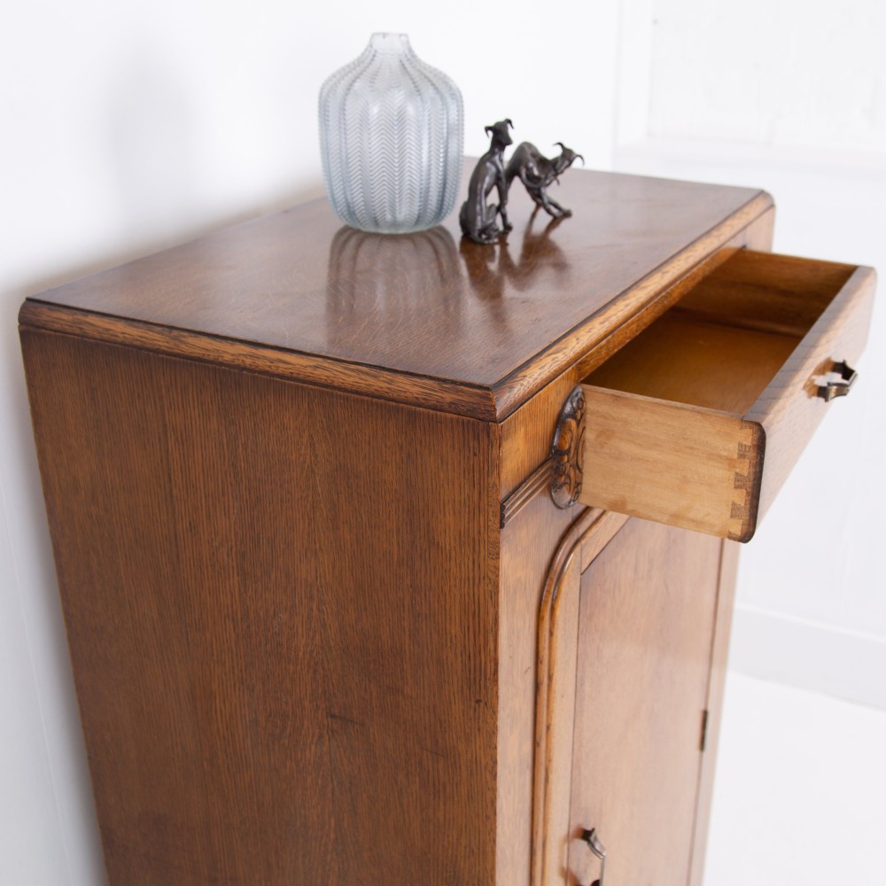 A 1930s Art Deco oak bachelors wardrobe featuring a top drawer, a central cupboard door with rounded framing, and carved corner accents. View V