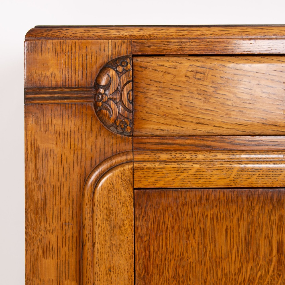 A 1930s Art Deco oak bachelors wardrobe featuring a top drawer, a central cupboard door with rounded framing, and carved corner accents. View VI