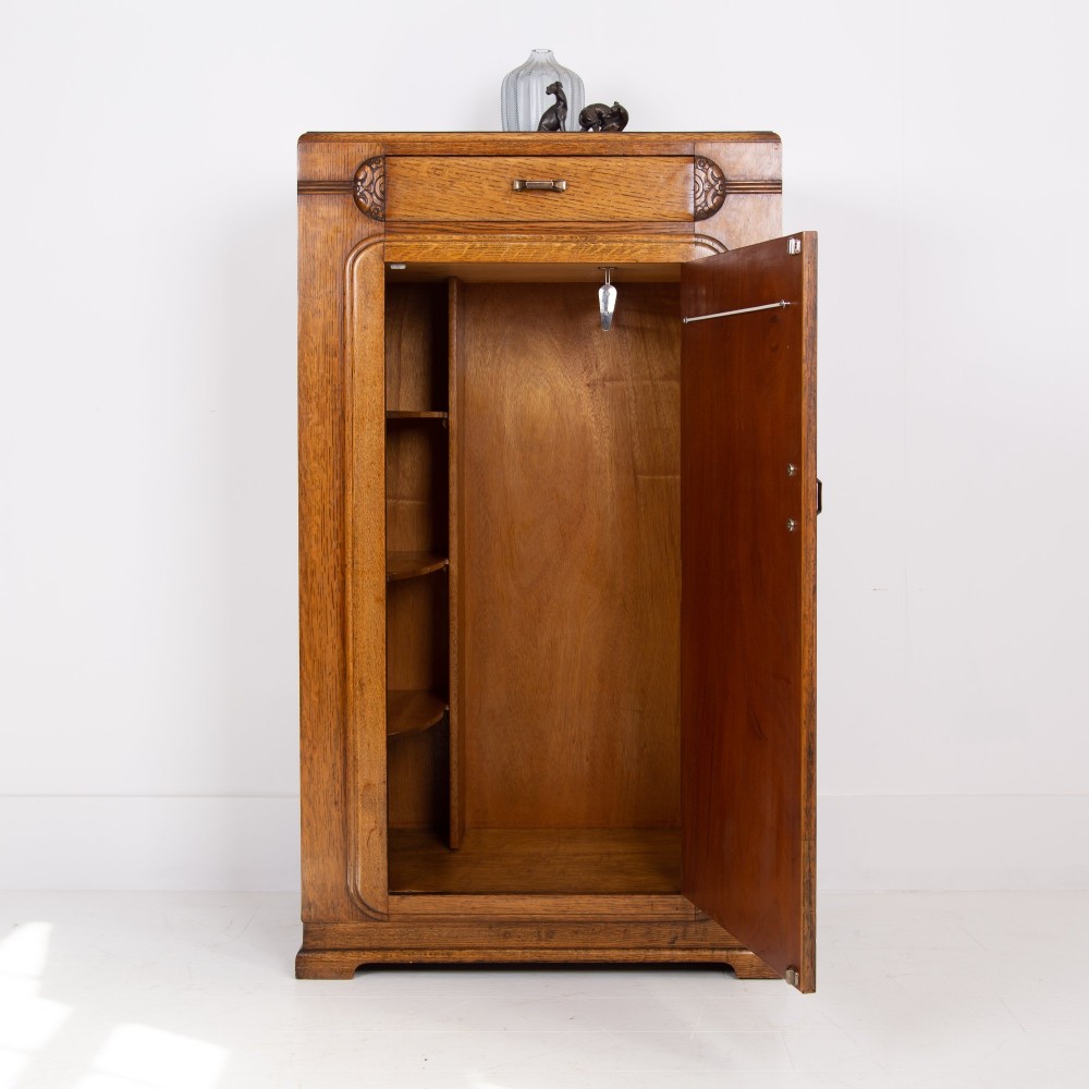 A 1930s Art Deco oak bachelors wardrobe featuring a top drawer, a central cupboard door with rounded framing, and carved corner accents. View XII