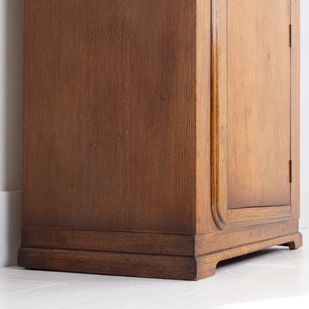 A 1930s Art Deco oak bachelors wardrobe featuring a top drawer, a central cupboard door with rounded framing, and carved corner accents. View XIII