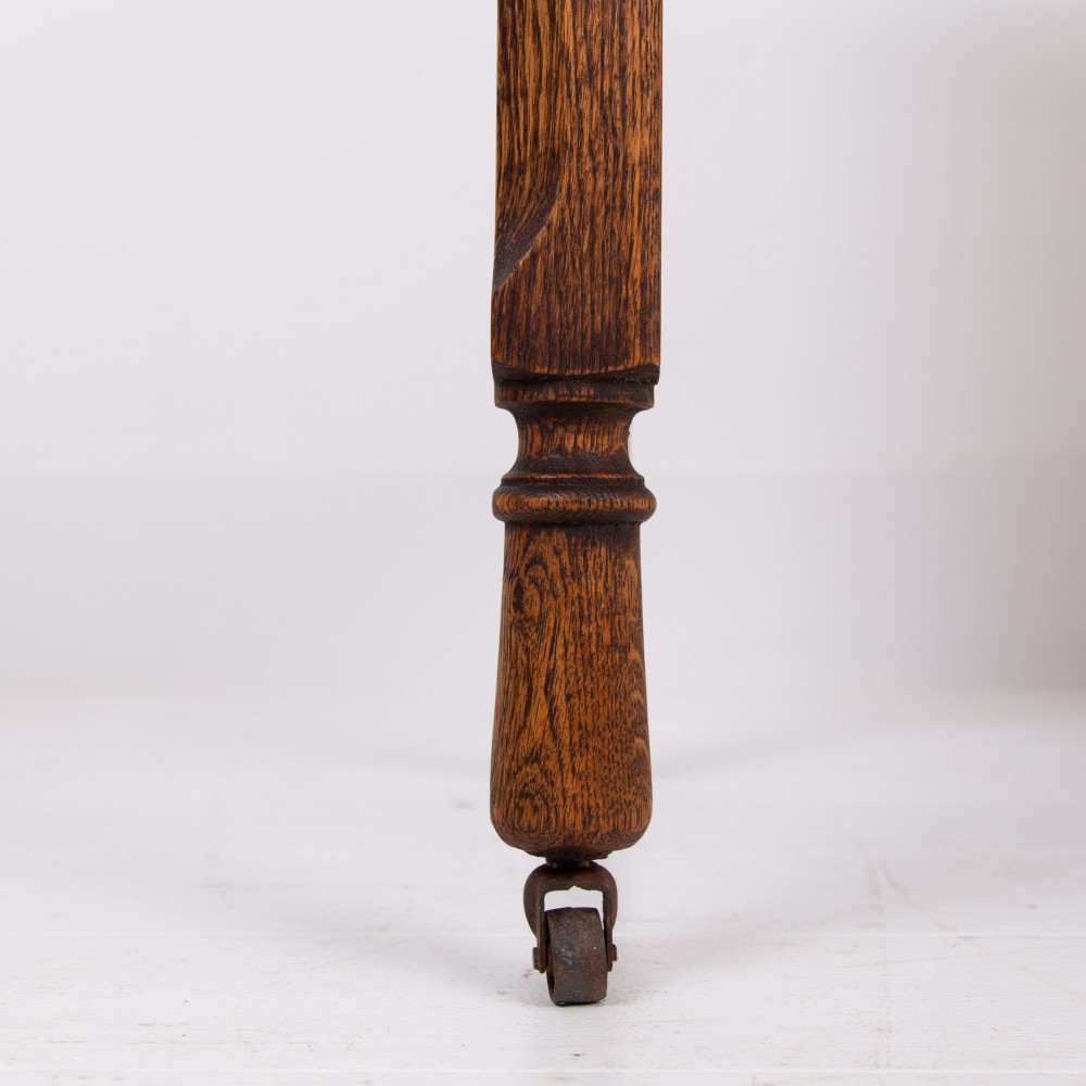 A golden oak writing desk featuring four drawers with brass drop handles, shaped kneehole brackets, turned legs, and metal castors. View VII