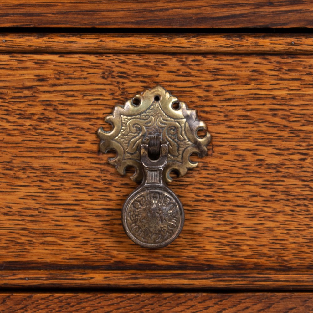 A golden oak writing desk featuring four drawers with brass drop handles, shaped kneehole brackets, turned legs, and metal castors. View XI