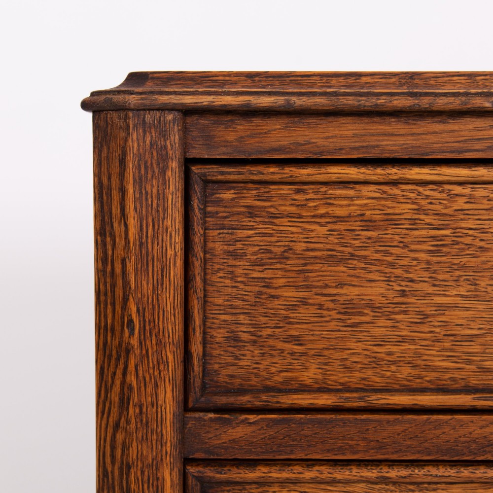 A golden oak writing desk featuring four drawers with brass drop handles, shaped kneehole brackets, turned legs, and metal castors. View XII