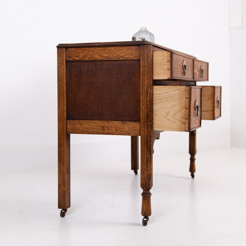 A golden oak writing desk featuring four drawers with brass drop handles, shaped kneehole brackets, turned legs, and metal castors. View XIII