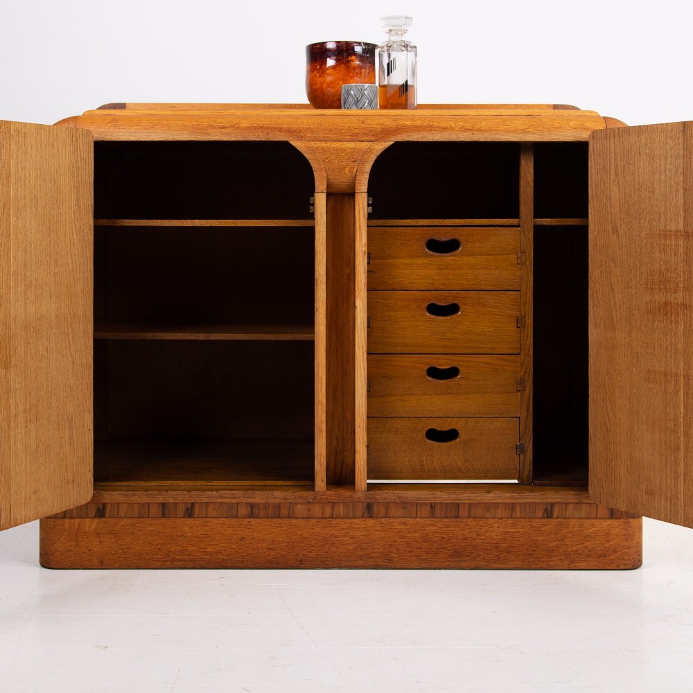 An Art Deco golden oak sideboard cabinet featuring rounded top edges, quarter-sawn wood grain, two central doors with wooden block handles, and a solid base plinth. View II