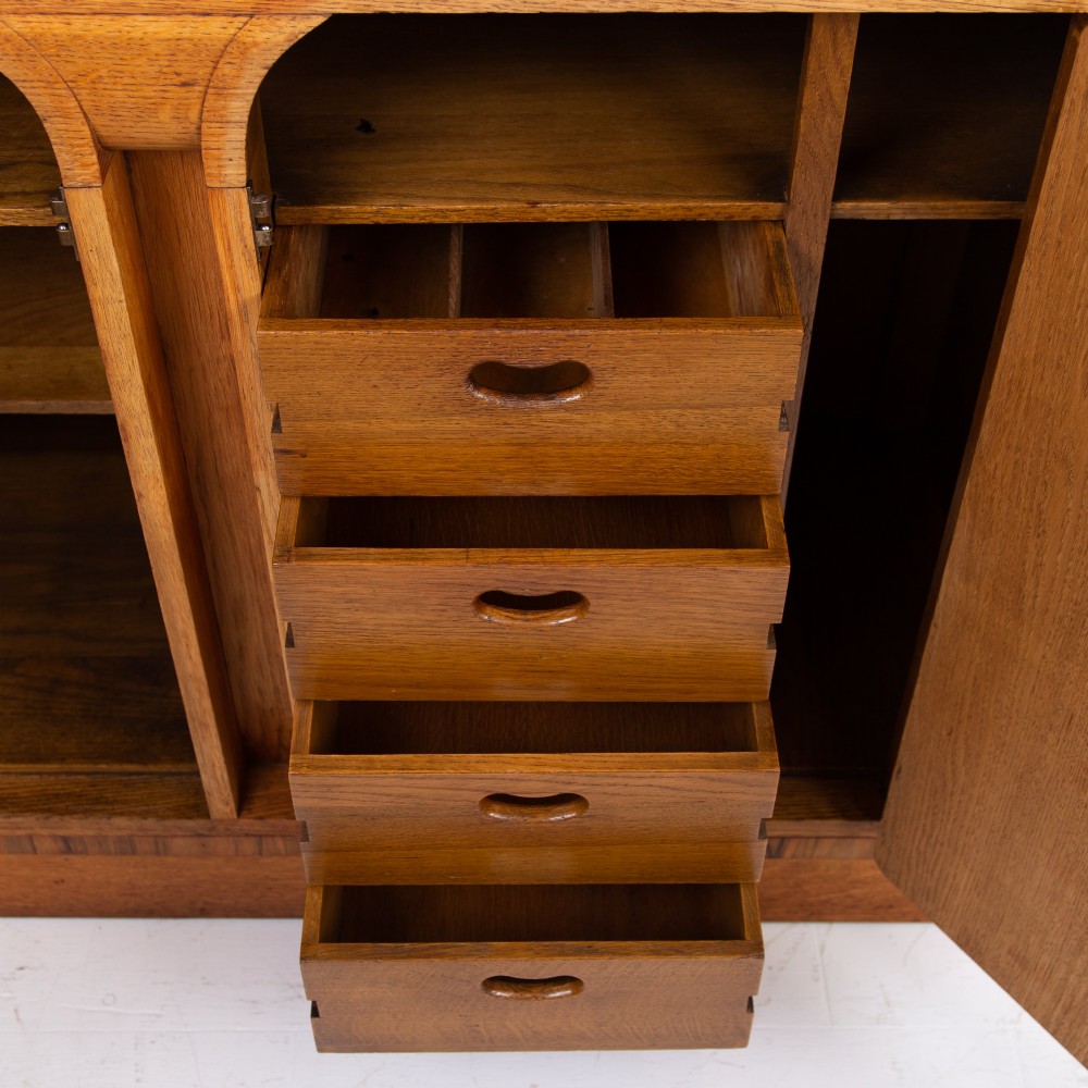 An Art Deco golden oak sideboard cabinet featuring rounded top edges, quarter-sawn wood grain, two central doors with wooden block handles, and a solid base plinth. View III