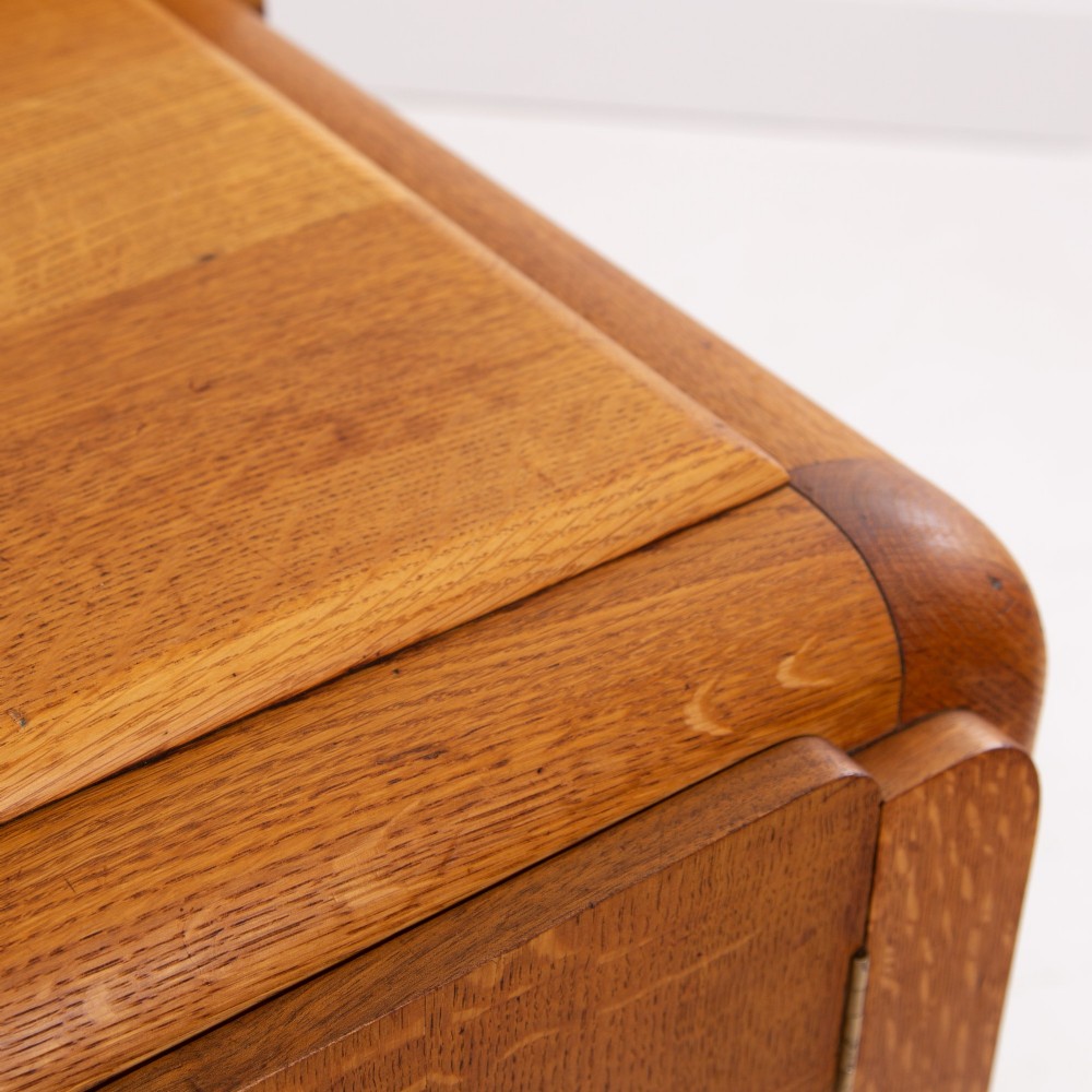 An Art Deco golden oak sideboard cabinet featuring rounded top edges, quarter-sawn wood grain, two central doors with wooden block handles, and a solid base plinth. View V