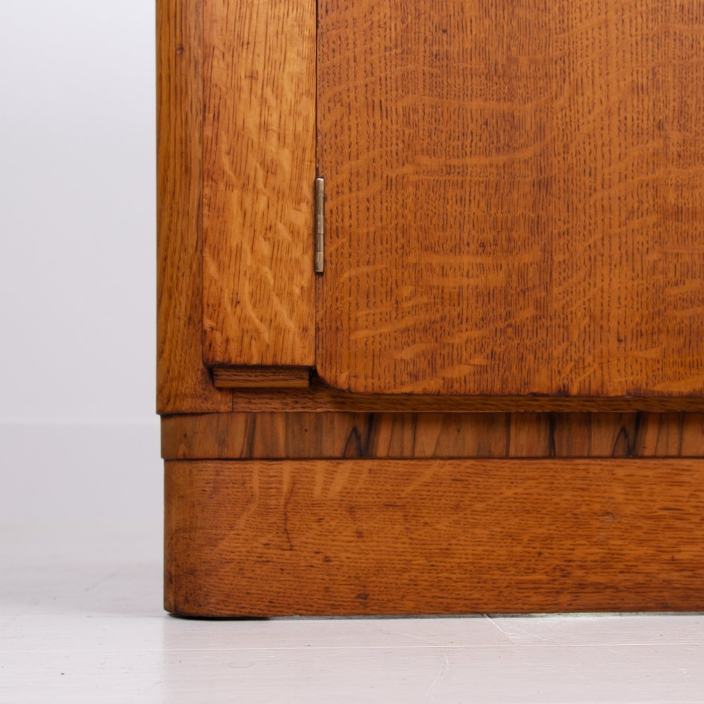 An Art Deco golden oak sideboard cabinet featuring rounded top edges, quarter-sawn wood grain, two central doors with wooden block handles, and a solid base plinth. View VIII