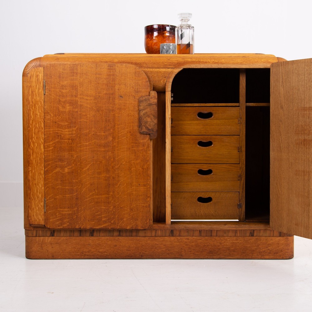 An Art Deco golden oak sideboard cabinet featuring rounded top edges, quarter-sawn wood grain, two central doors with wooden block handles, and a solid base plinth. View XII