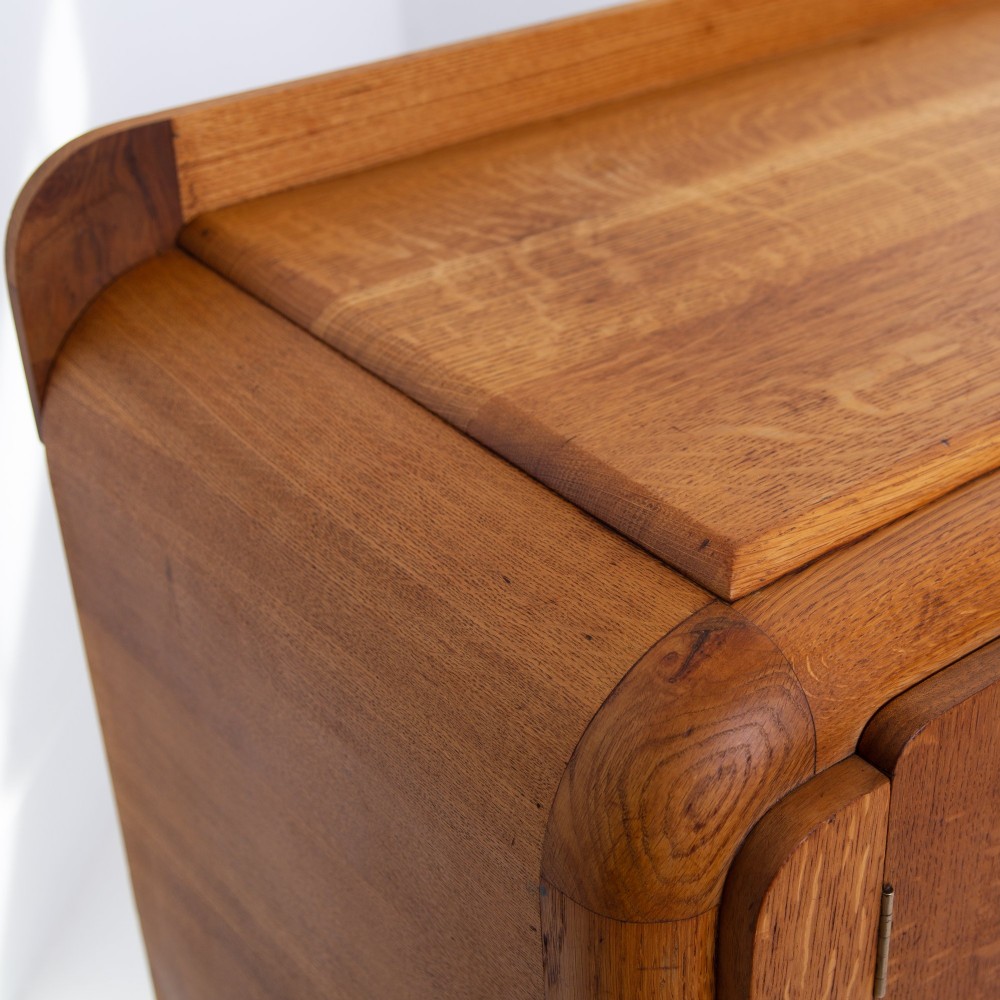 An Art Deco golden oak sideboard cabinet featuring rounded top edges, quarter-sawn wood grain, two central doors with wooden block handles, and a solid base plinth. View XIII