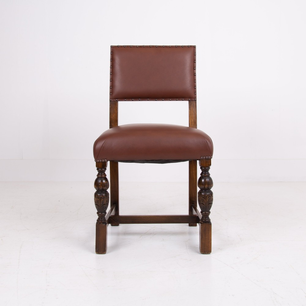 A set of six dark oak dining chairs featuring brown leather upholstered seats and backrests with brass stud detailing and turned front legs. View V