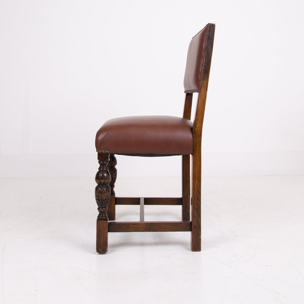 A set of six dark oak dining chairs featuring brown leather upholstered seats and backrests with brass stud detailing and turned front legs. View VI