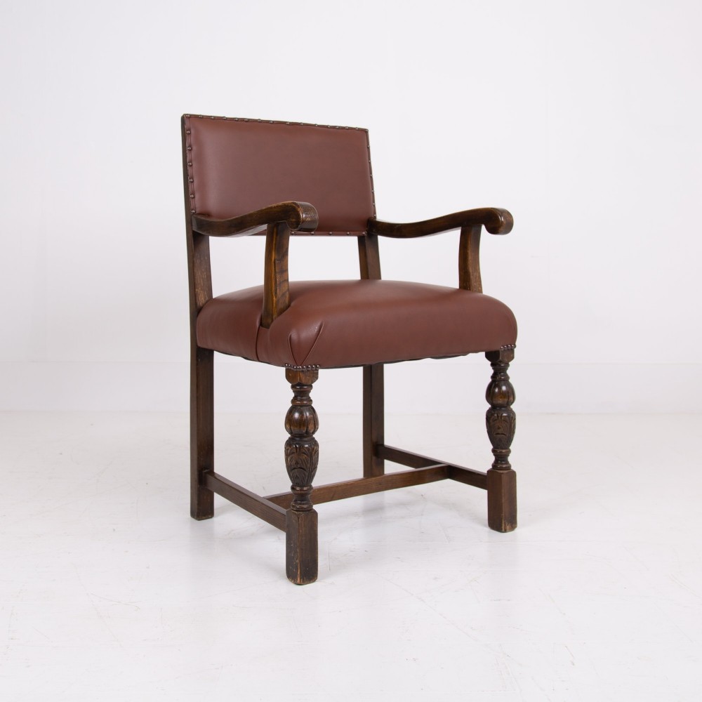A set of six dark oak dining chairs featuring brown leather upholstered seats and backrests with brass stud detailing and turned front legs. View X