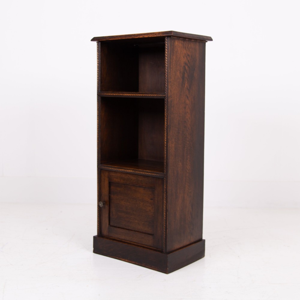 A small late Victorian dark oak bookcase featuring two open shelves above a single cupboard door with carved rope-twist moulding and a solid plinth base.