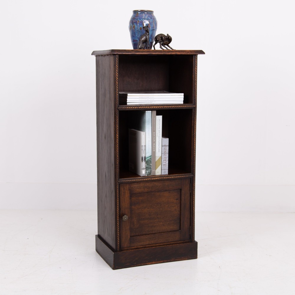 A small late Victorian dark oak bookcase featuring two open shelves above a single cupboard door with carved rope-twist moulding and a solid plinth base. View II