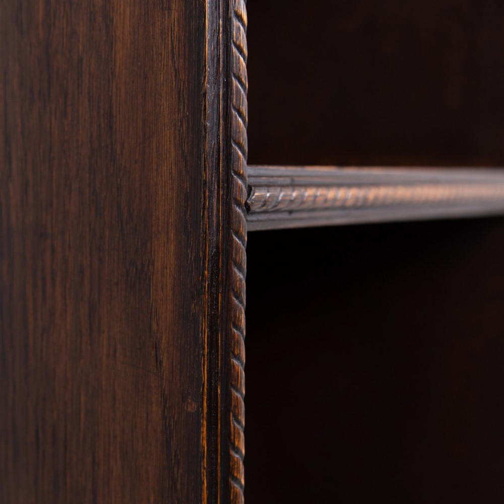 A small late Victorian dark oak bookcase featuring two open shelves above a single cupboard door with carved rope-twist moulding and a solid plinth base. View IV