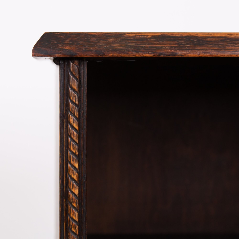 A small late Victorian dark oak bookcase featuring two open shelves above a single cupboard door with carved rope-twist moulding and a solid plinth base. View V