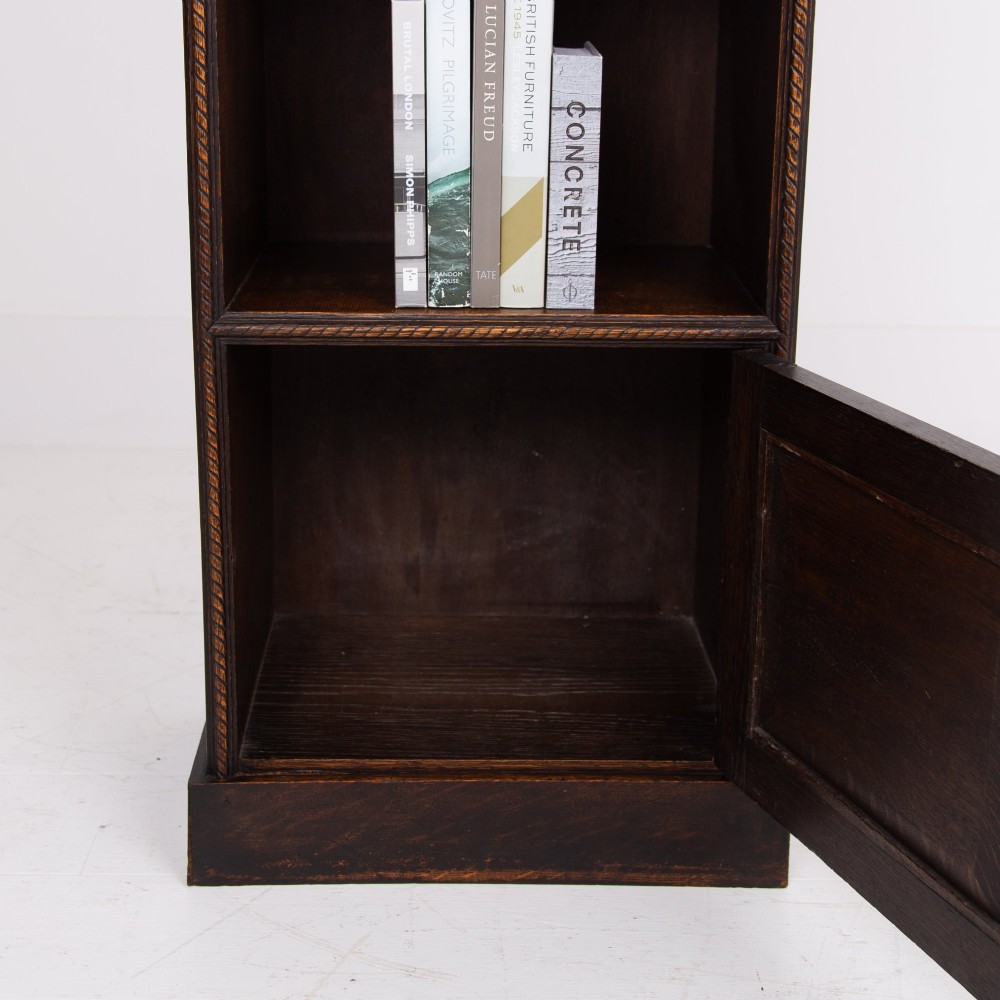A small late Victorian dark oak bookcase featuring two open shelves above a single cupboard door with carved rope-twist moulding and a solid plinth base. View VI