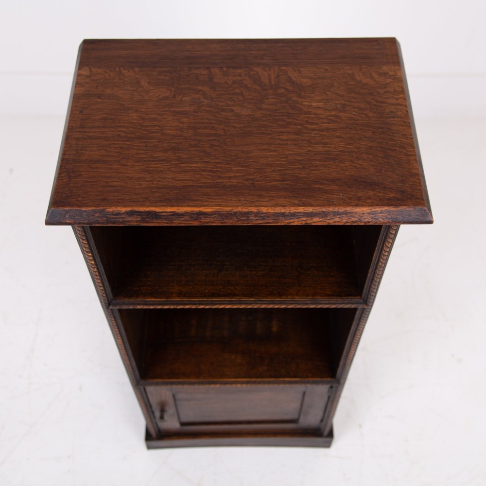 A small late Victorian dark oak bookcase featuring two open shelves above a single cupboard door with carved rope-twist moulding and a solid plinth base. View IX
