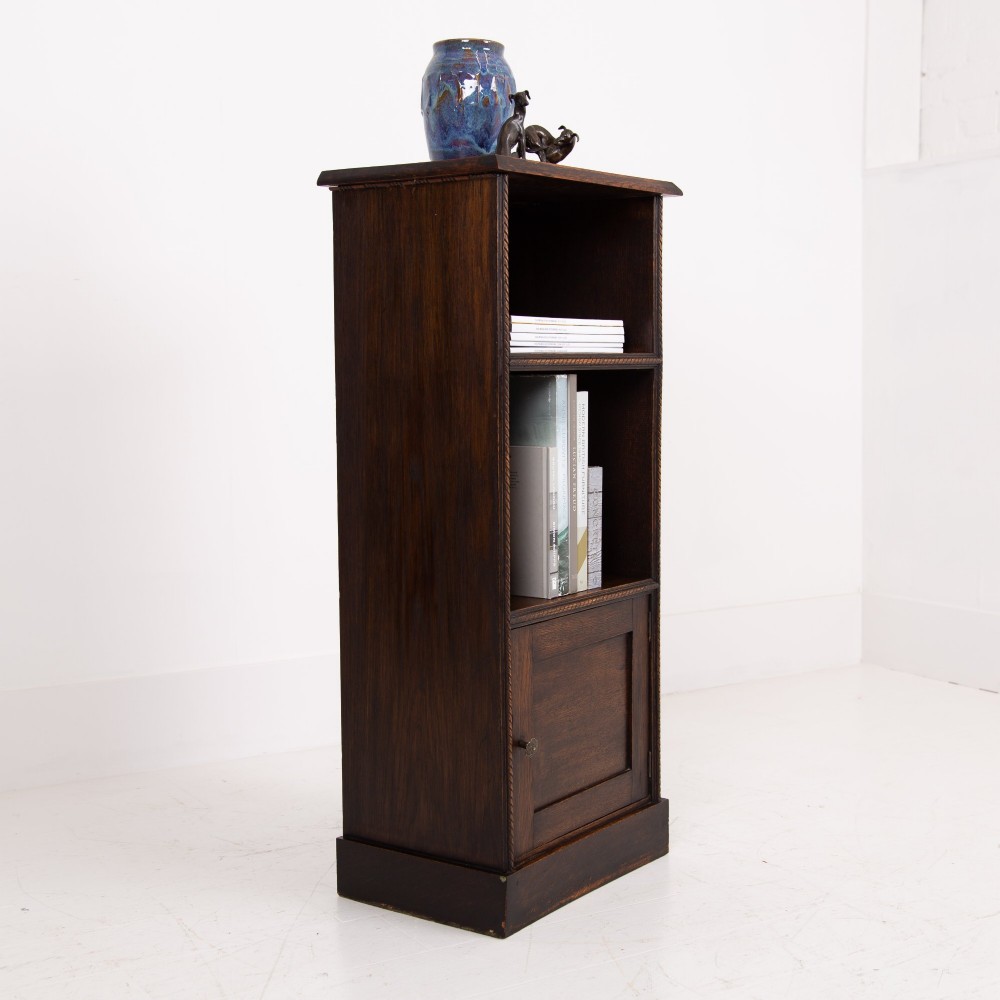 A small late Victorian dark oak bookcase featuring two open shelves above a single cupboard door with carved rope-twist moulding and a solid plinth base. View XII