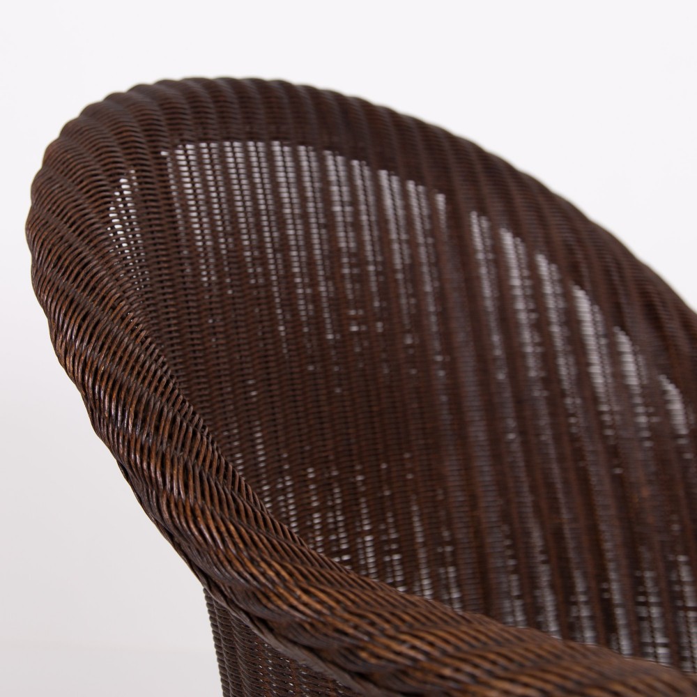 A 1930s dark brown Lloyd Loom woven armchair featuring carved oak armrests, turned front legs, and a patterned seat cushion. View VIII