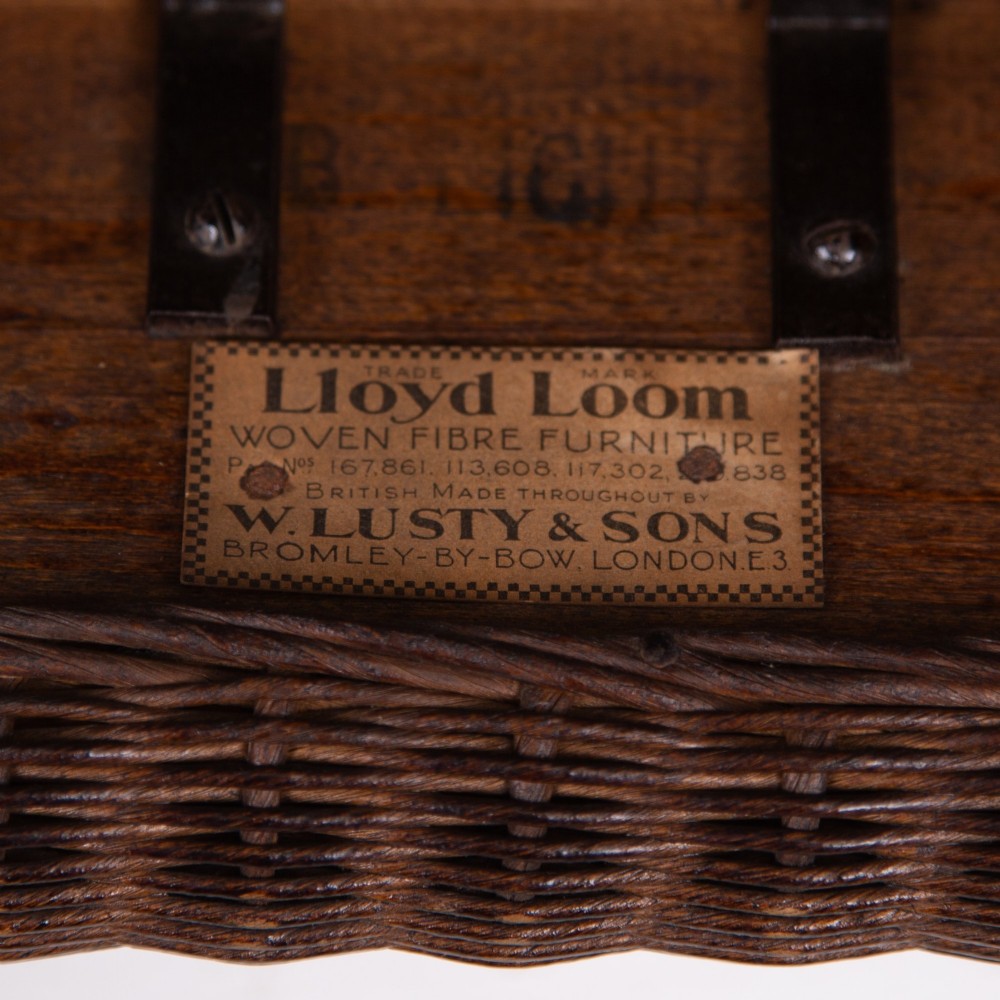 A 1930s dark brown Lloyd Loom woven armchair featuring carved oak armrests, turned front legs, and a patterned seat cushion. View XI