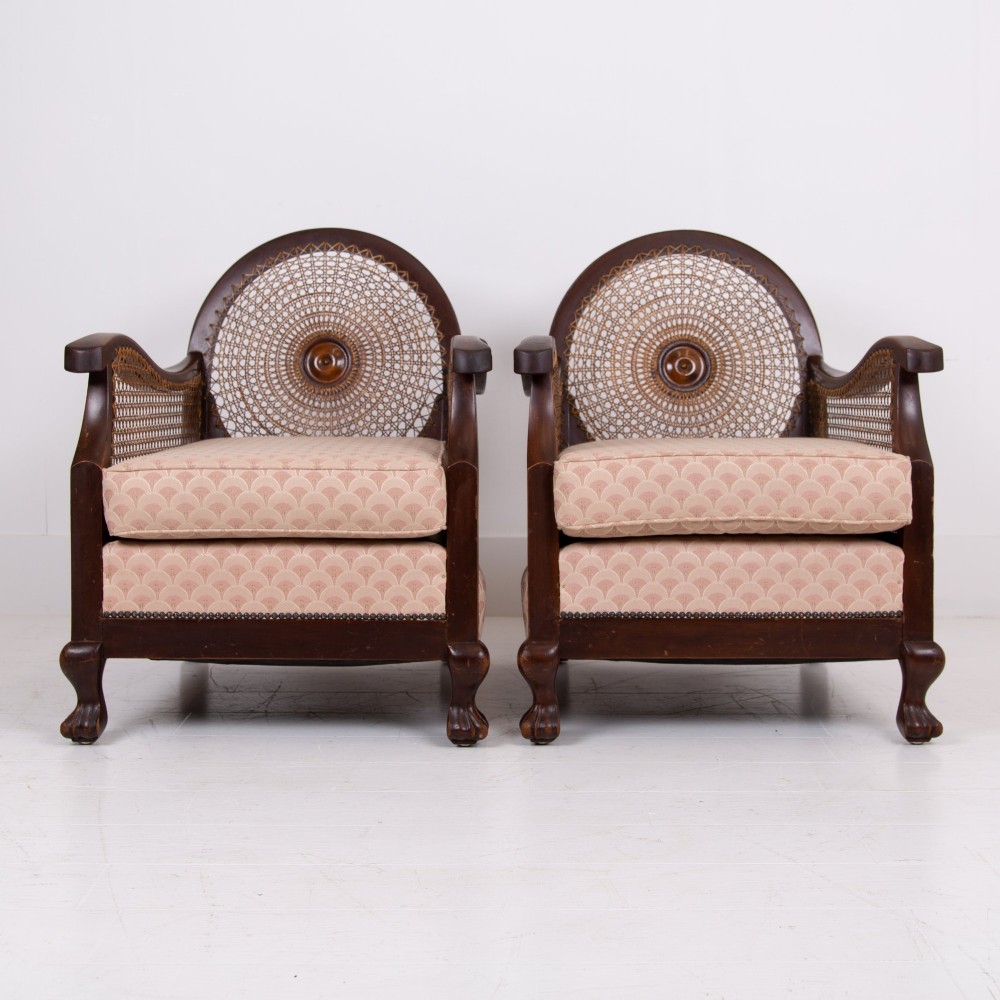 A pair of 1920s dark wood bergere armchairs featuring circular woven cane backs, cane sides, and pink fan-pattern upholstered cushions. View II
