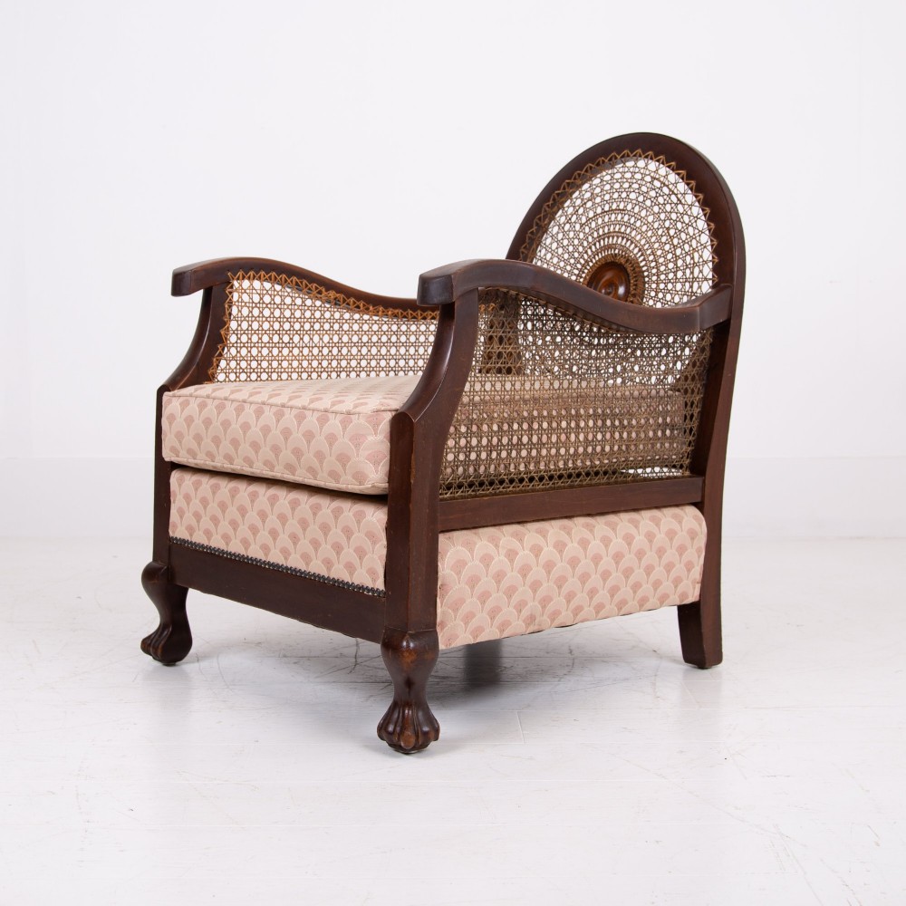 A pair of 1920s dark wood bergere armchairs featuring circular woven cane backs, cane sides, and pink fan-pattern upholstered cushions. View V