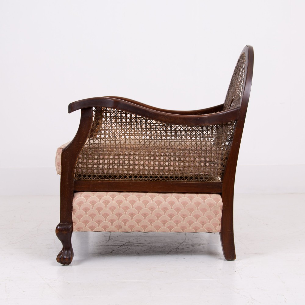 A pair of 1920s dark wood bergere armchairs featuring circular woven cane backs, cane sides, and pink fan-pattern upholstered cushions. View VI