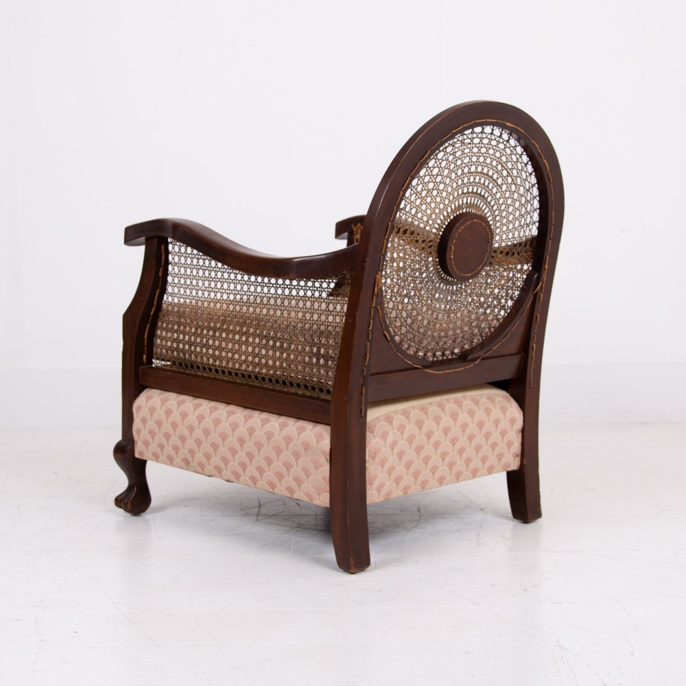 A pair of 1920s dark wood bergere armchairs featuring circular woven cane backs, cane sides, and pink fan-pattern upholstered cushions. View VII