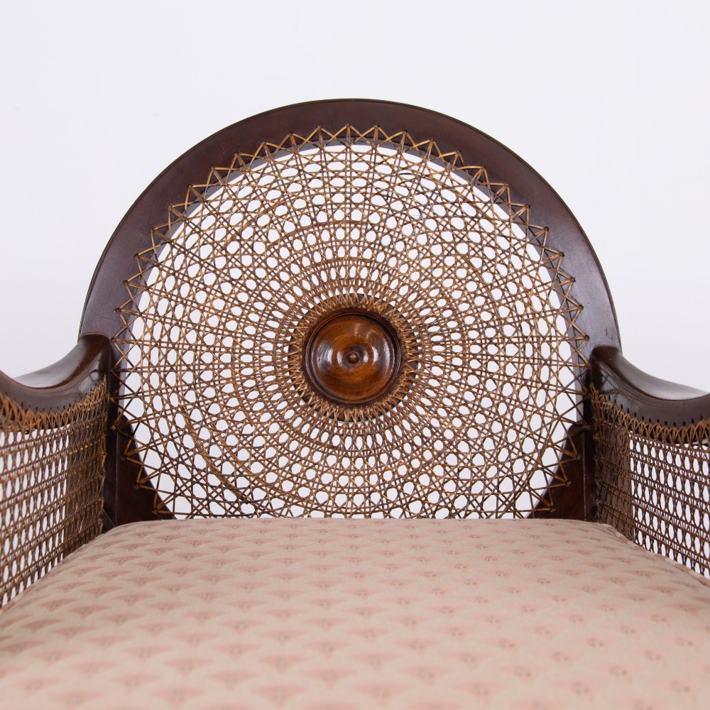 A pair of 1920s dark wood bergere armchairs featuring circular woven cane backs, cane sides, and pink fan-pattern upholstered cushions. View IX