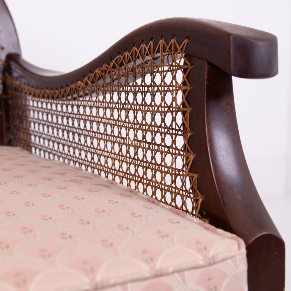A pair of 1920s dark wood bergere armchairs featuring circular woven cane backs, cane sides, and pink fan-pattern upholstered cushions. View X