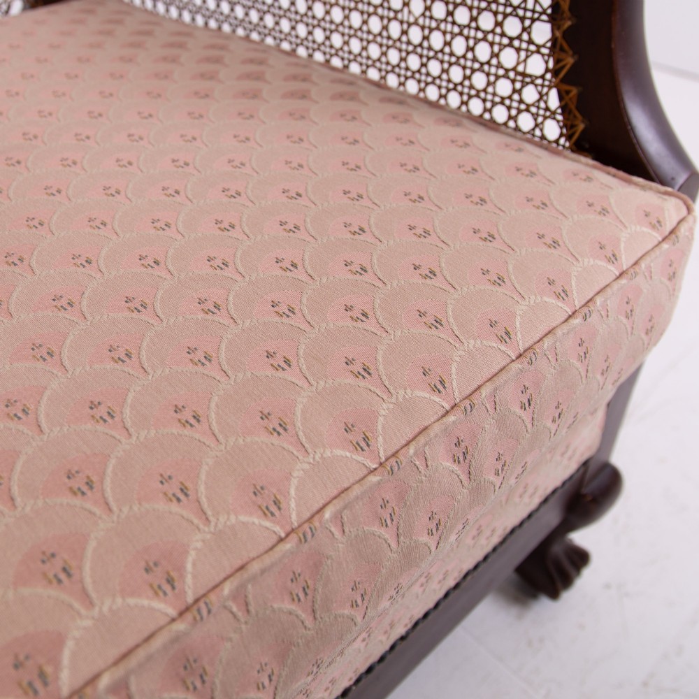 A pair of 1920s dark wood bergere armchairs featuring circular woven cane backs, cane sides, and pink fan-pattern upholstered cushions. View XIV