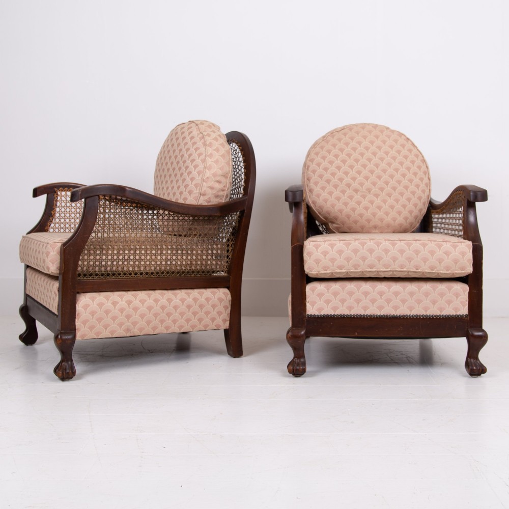 A pair of 1920s dark wood bergere armchairs featuring circular woven cane backs, cane sides, and pink fan-pattern upholstered cushions. View XV