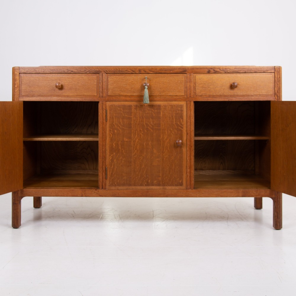 A 1930s light oak sideboard featuring three upper drawers over three panelled cupboard doors with wooden knob handles. View V