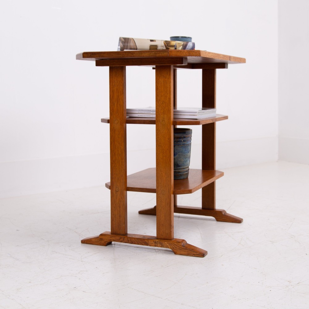 An antique Cotswold School solid oak side table featuring three rectangular shelves supported by straight uprights and sled feet. View II