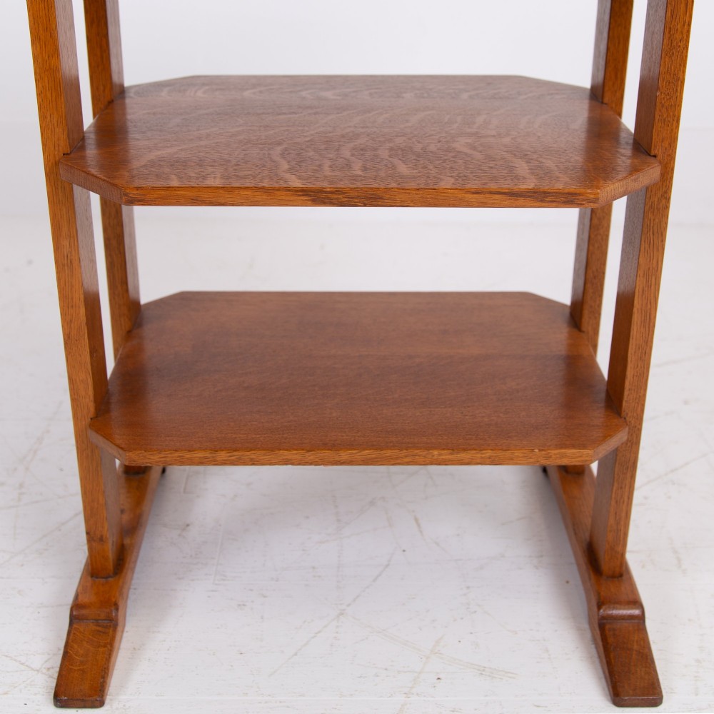 An antique Cotswold School solid oak side table featuring three rectangular shelves supported by straight uprights and sled feet. View VI