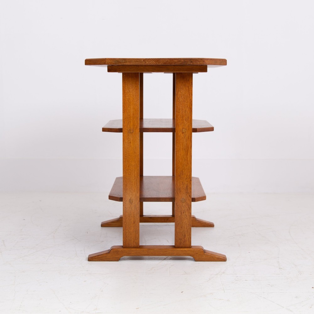 An antique Cotswold School solid oak side table featuring three rectangular shelves supported by straight uprights and sled feet. View VII