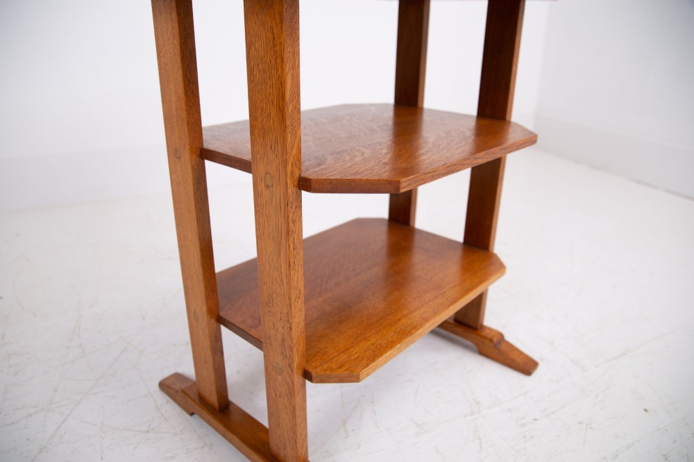 An antique Cotswold School solid oak side table featuring three rectangular shelves supported by straight uprights and sled feet. View XII