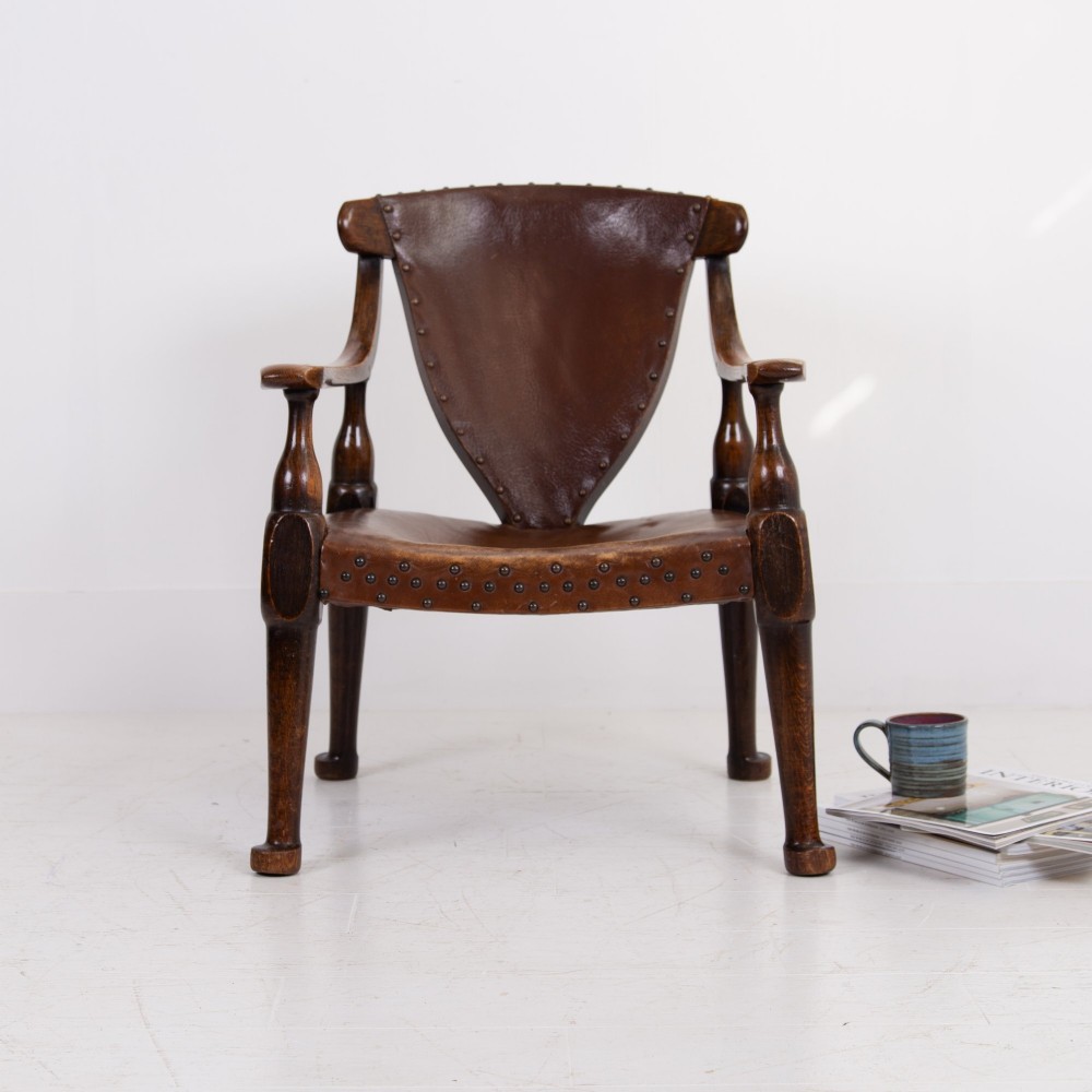 An Arts and Crafts style dark oak armchair featuring turned front legs, wide curved armrests, and brown studded leather upholstery. View II