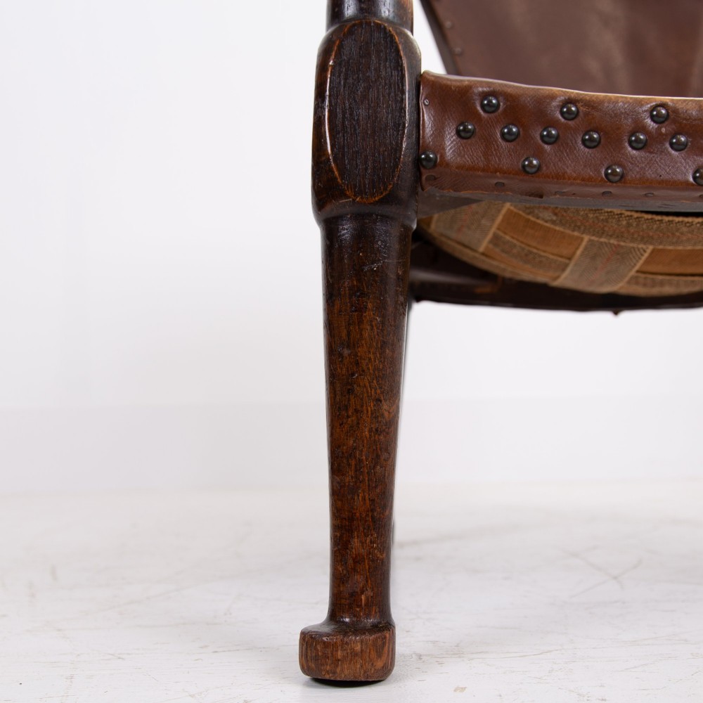 An Arts and Crafts style dark oak armchair featuring turned front legs, wide curved armrests, and brown studded leather upholstery. View VII