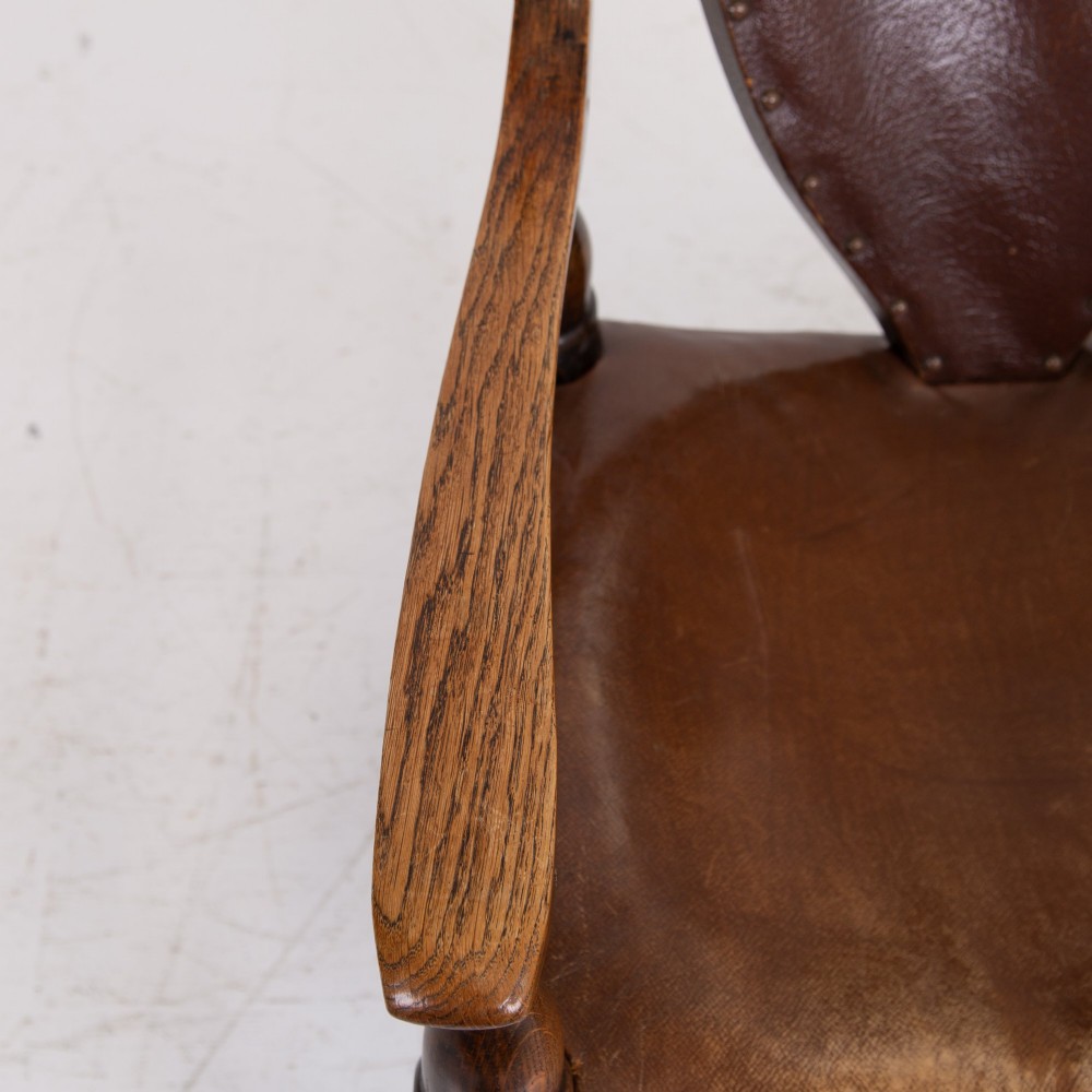 An Arts and Crafts style dark oak armchair featuring turned front legs, wide curved armrests, and brown studded leather upholstery. View XI