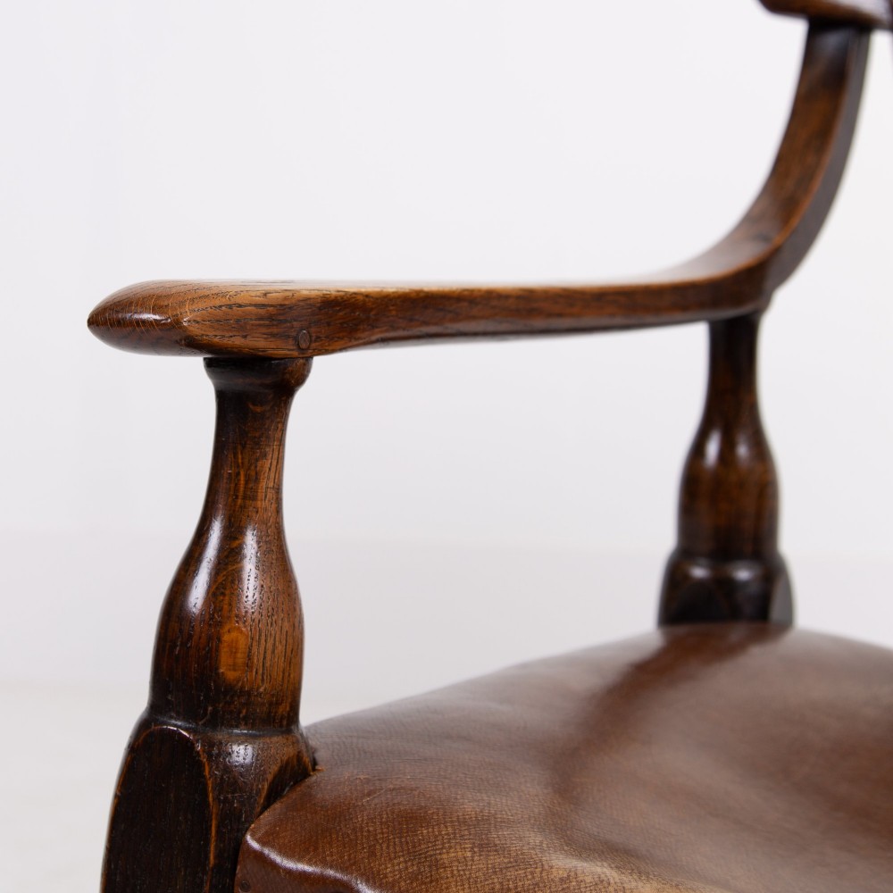 An Arts and Crafts style dark oak armchair featuring turned front legs, wide curved armrests, and brown studded leather upholstery. View XIII