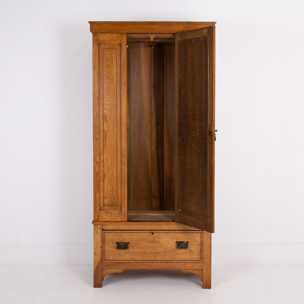 An Edwardian single-door oak wardrobe featuring a central vertical mirror, recessed side panels, a single base drawer, and a stepped top cornice. View V