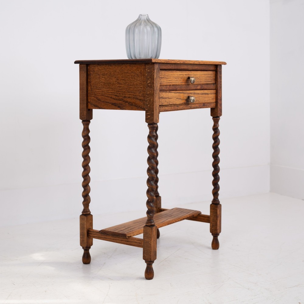 A warm brown oak side table featuring two stacked drawers with metal shell handles, four turned barley twist legs, and a low rectangular shelf. View II
