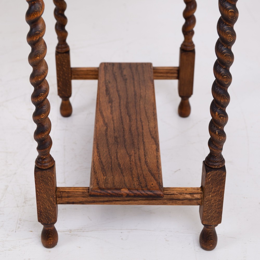 A warm brown oak side table featuring two stacked drawers with metal shell handles, four turned barley twist legs, and a low rectangular shelf. View X