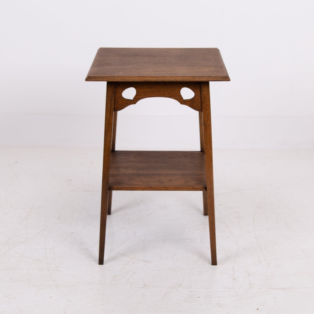 An Arts and Crafts solid oak two-tier side table with tapered legs and heart-shaped pierced motifs along the apron. View II