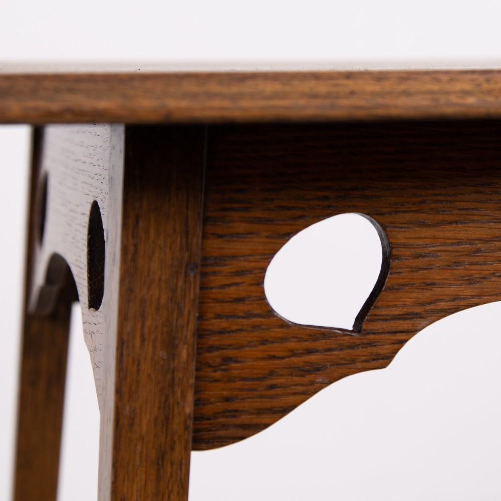 An Arts and Crafts solid oak two-tier side table with tapered legs and heart-shaped pierced motifs along the apron. View V