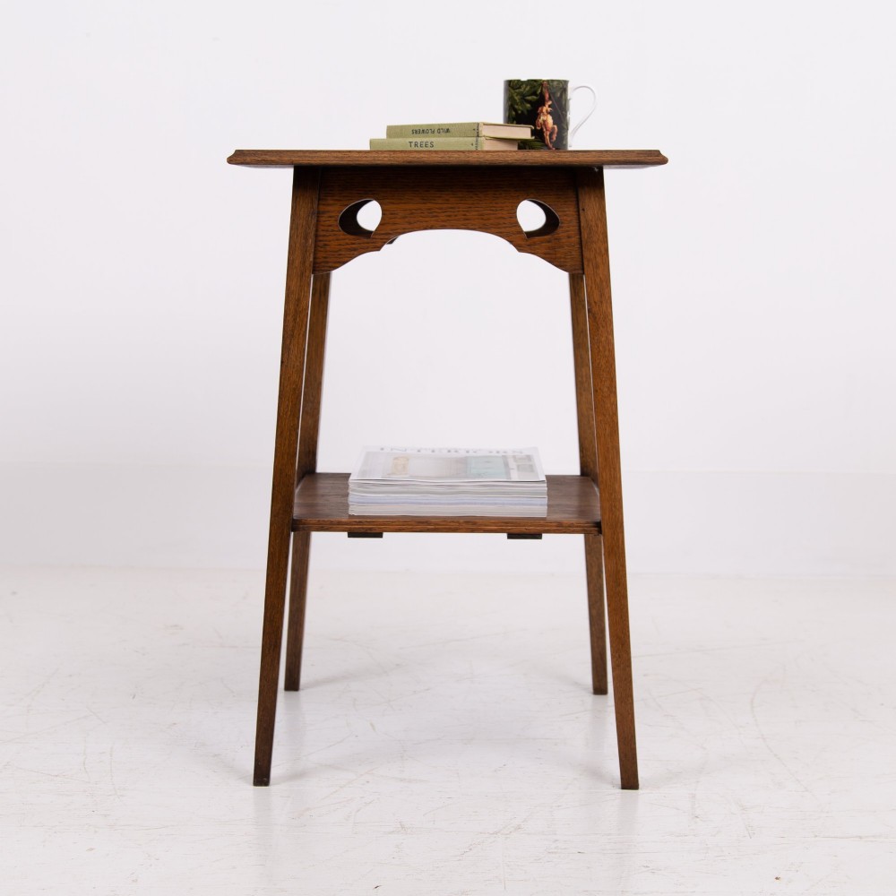 An Arts and Crafts solid oak two-tier side table with tapered legs and heart-shaped pierced motifs along the apron. View XII